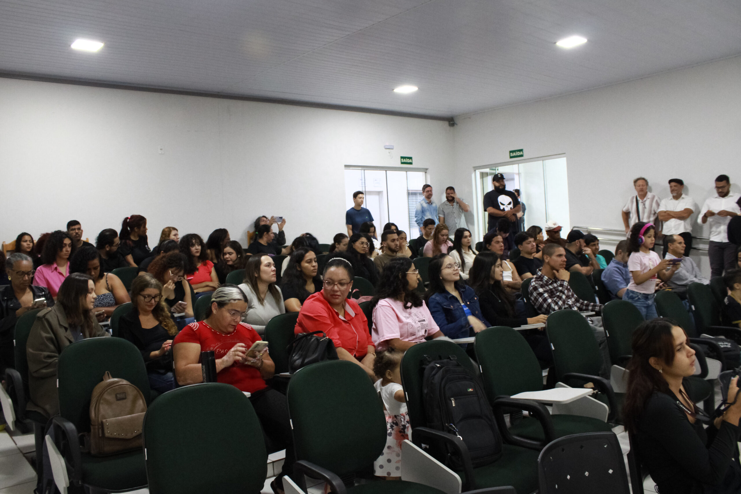 Grupo de pessoas sentadas e algumas em pé em um auditório.