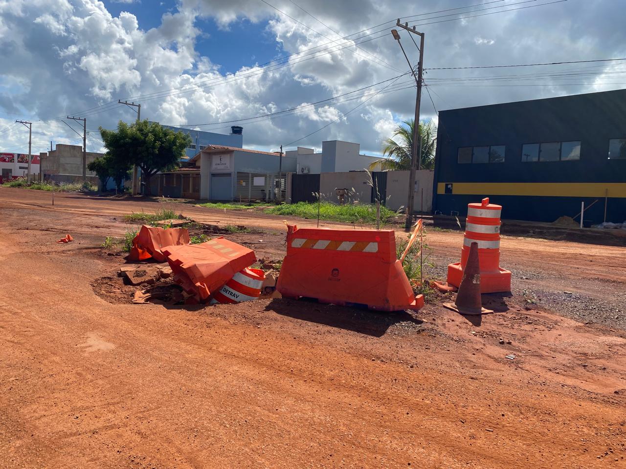Rua com buracos, com sinalização de cones laranjas jogados pelo chão atrapalhando a locomoção dos moradores e visitantes.