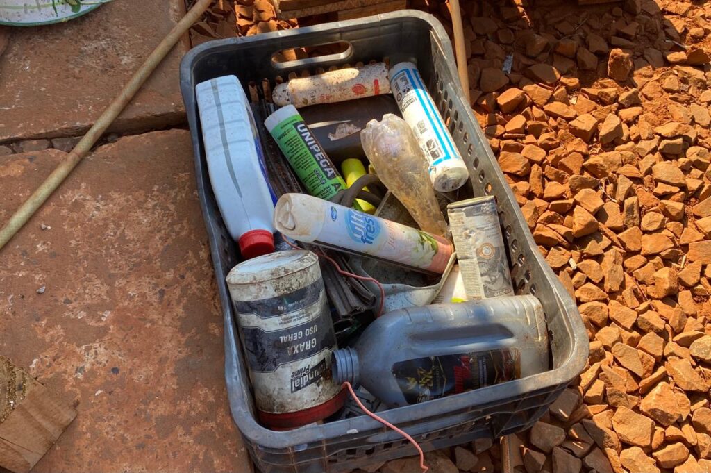 A imagem é composta por uma cestinha de supermercado, de cor preta. A mesma está cheia de produtos como embalagem de aerossol, aromatizador de ambiente e frascos de óleos automotivos.